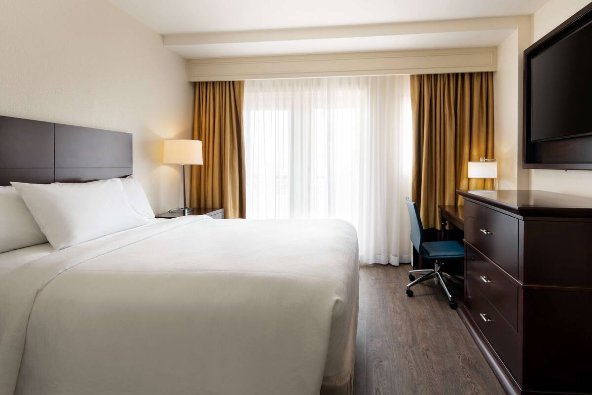 Een hotelkamer met een groot bed, een bureau met stoel, een televisie en een kledingkast.