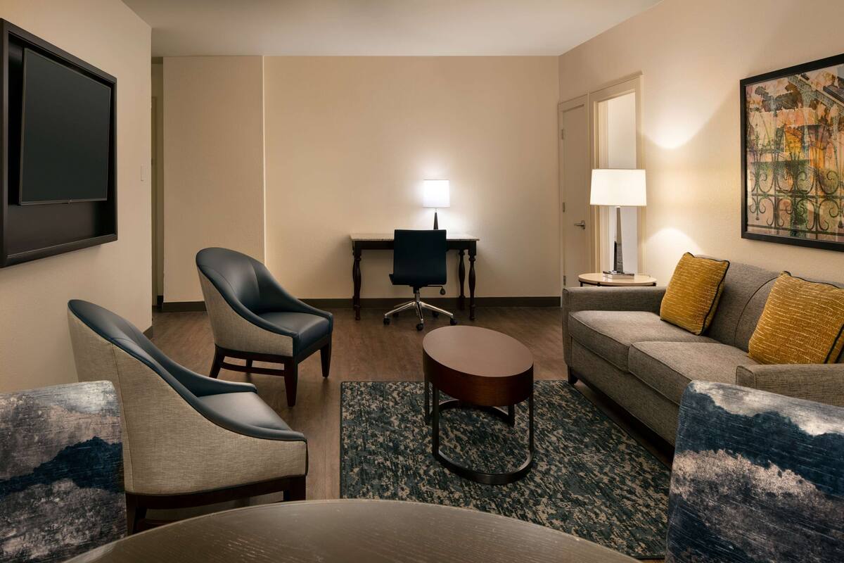 Een hotelkamer met een zithoek, een bureau, een televisie en een schilderij aan de muur.