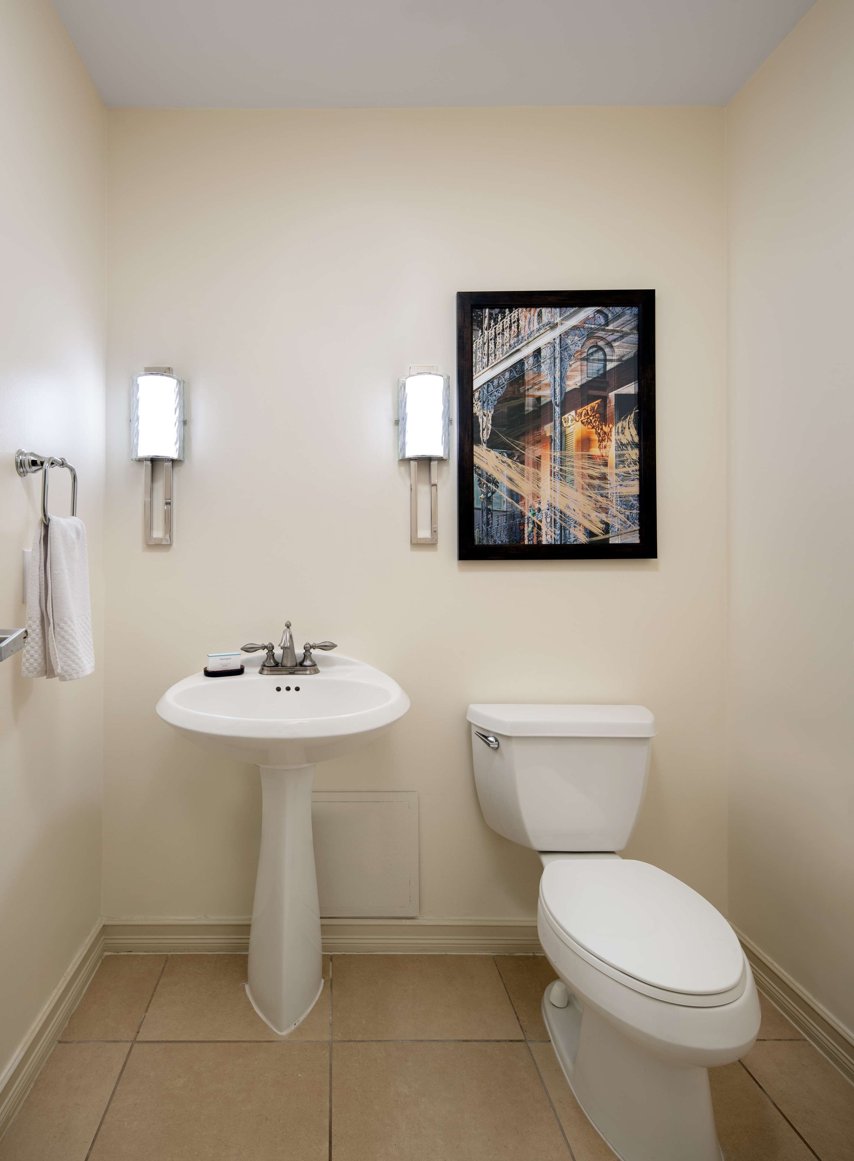 A bathroom with a pedestal sink, a toilet, and two wall-mounted lights.