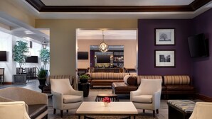 A spacious living area with a sofa set, armchairs, a coffee table, and a bar area in the background. - Embassy Suites by Hilton New Orleans (New Orleans)
