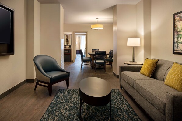 A hotel room with a sofa, armchair, dining table, and a TV mounted on the wall.