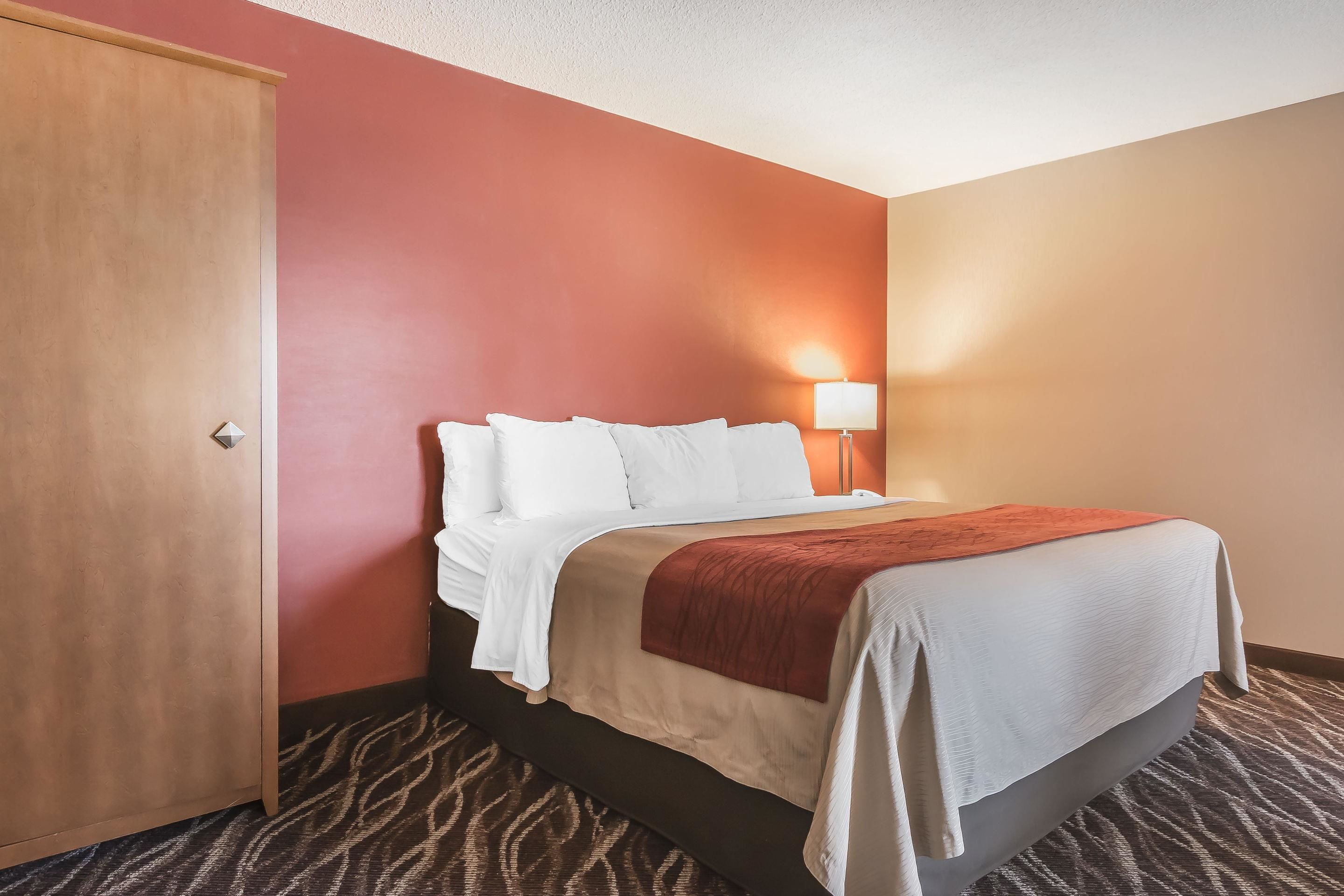 A hotel room with a bed, a nightstand, a lamp, and a door.