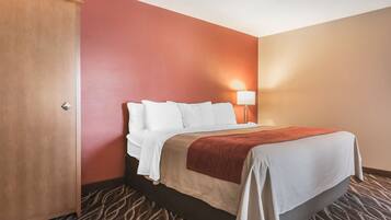 A hotel room with a bed, a nightstand, a lamp, and a door.