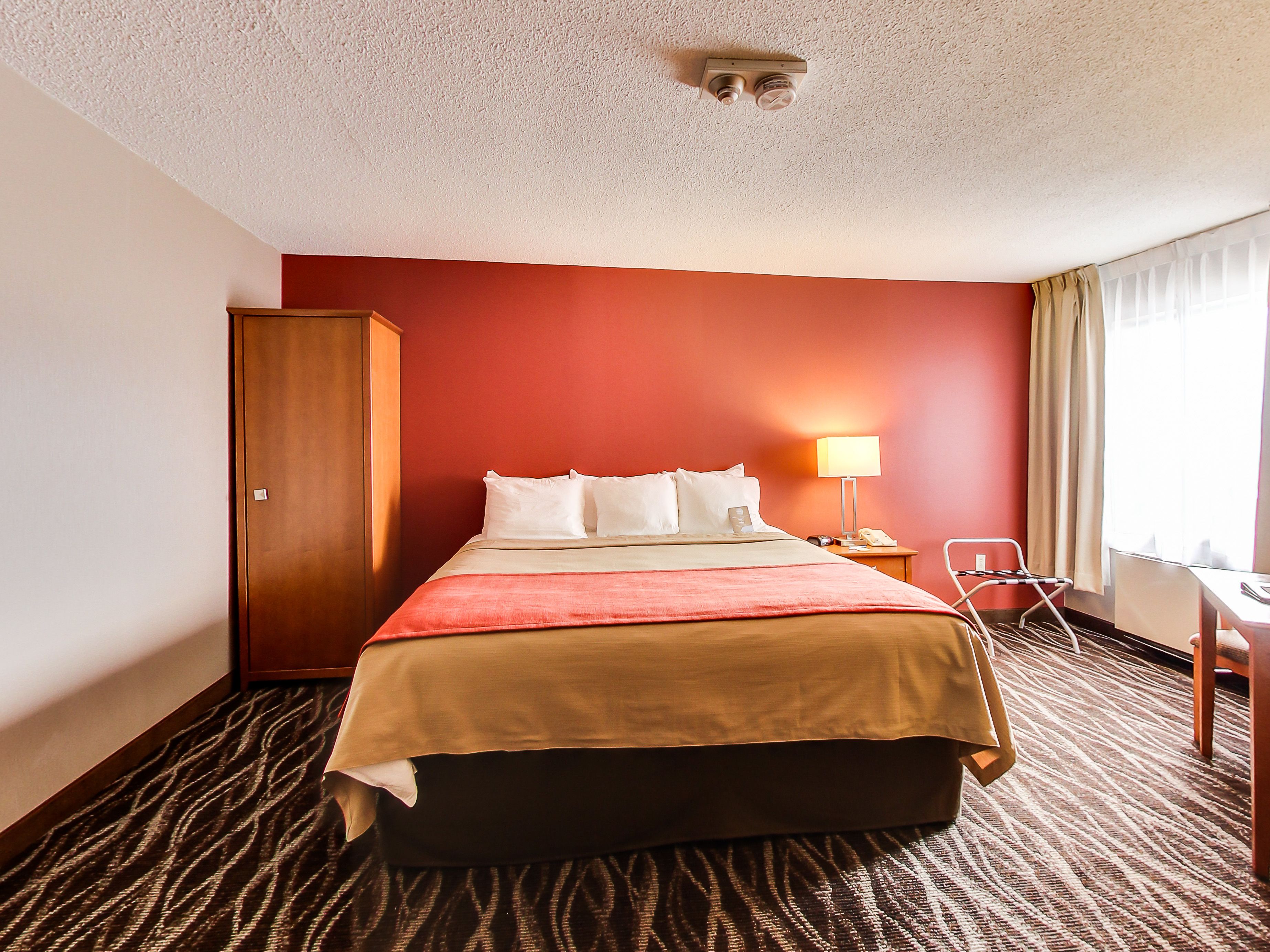 A hotel room with a bed, a wardrobe, a desk, and a chair.