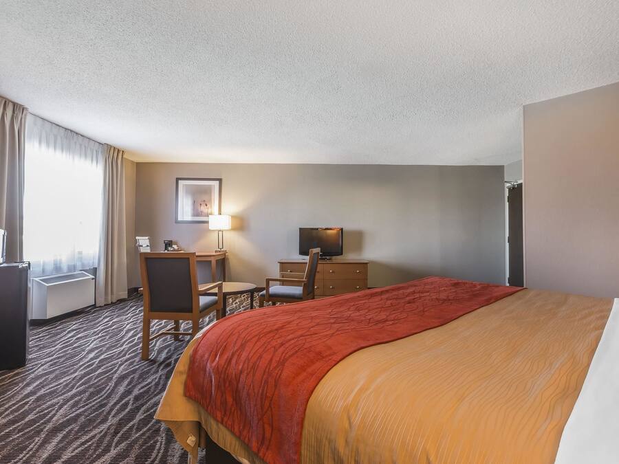 Habitación de hotel con una cama grande, un escritorio con silla, un televisor y una ventana con cortinas.
