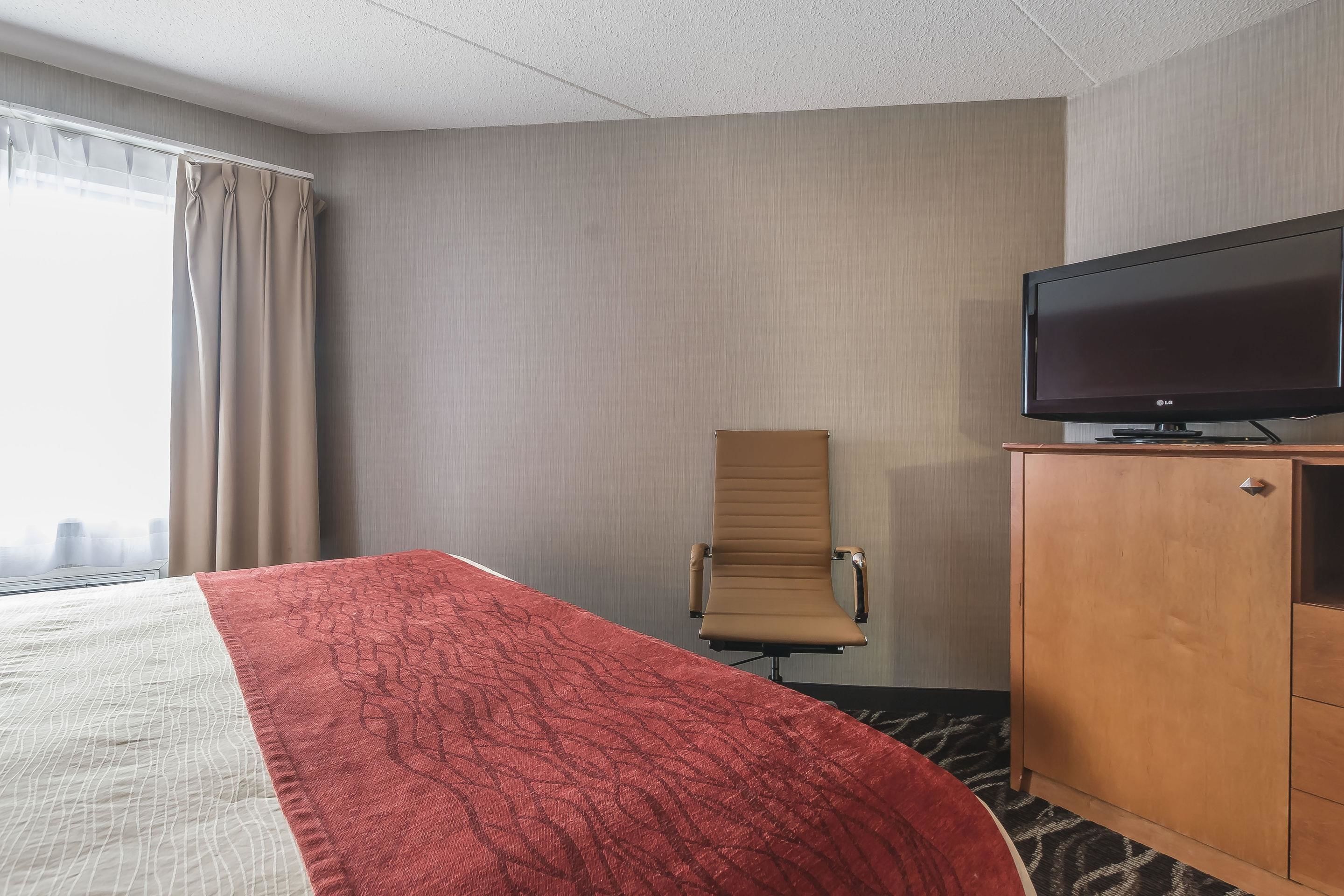 A hotel room with a bed, a television on a wooden cabinet, a chair, and a window with curtains.