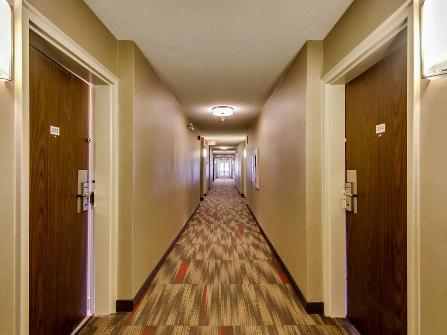 A hotel hallway with carpeted floors, wooden doors, and numbered doorplates.