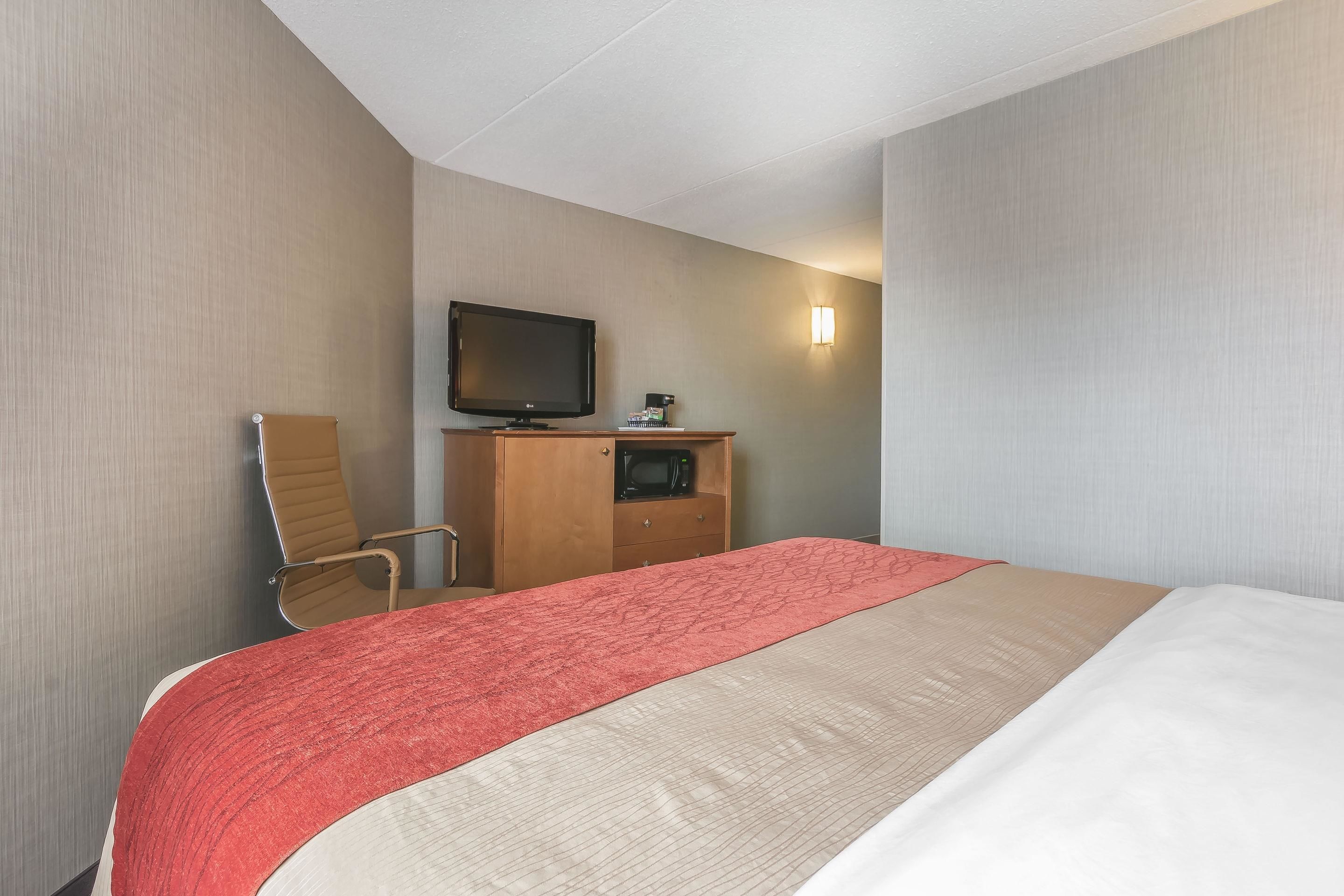 A hotel room with a bed, a television, a desk with a microwave, and a chair.