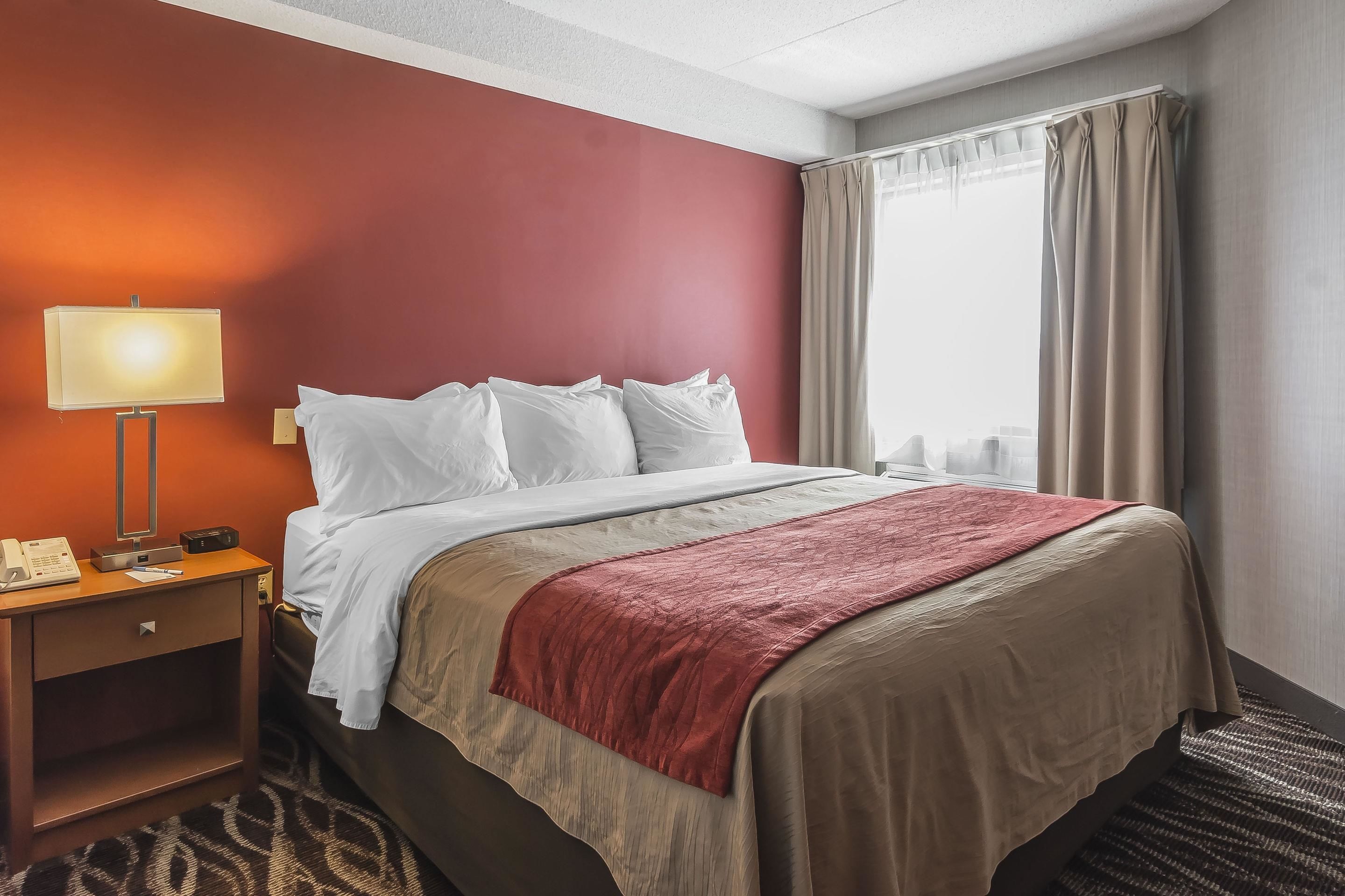 A hotel room with a bed, a nightstand with a lamp, a telephone, and a window with curtains.