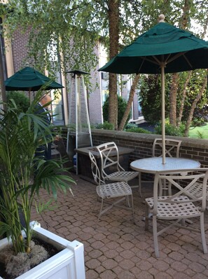 An outdoor patio with a brick floor, white metal chairs, a round table, and two green umbrellas. - Four Points by Sheraton Wakefield Boston Htl&Conference Cntr (Wakefield)