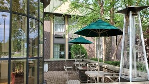 Eine Terrasse im Freien mit Glaswänden, Gartenmöbeln und grünen Sonnenschirmen.