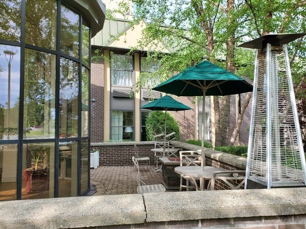 An outdoor patio with glass walls, outdoor seating, and green umbrellas. - Four Points by Sheraton Wakefield Boston Htl&Conference Cntr (Wakefield)