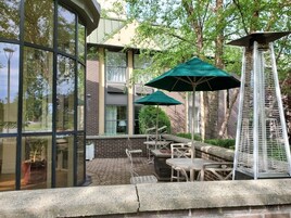 Un patio exterior con paredes de vidrio, mobiliario para exteriores y sombrillas verdes.