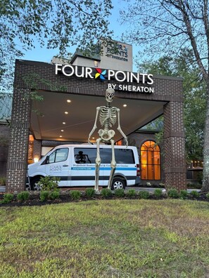 A building with a skeleton sculpture in front, a van with "Four Points by Sheraton" branding, and a sign above the entrance. - Four Points by Sheraton Wakefield Boston Htl&Conference Cntr (Wakefield)