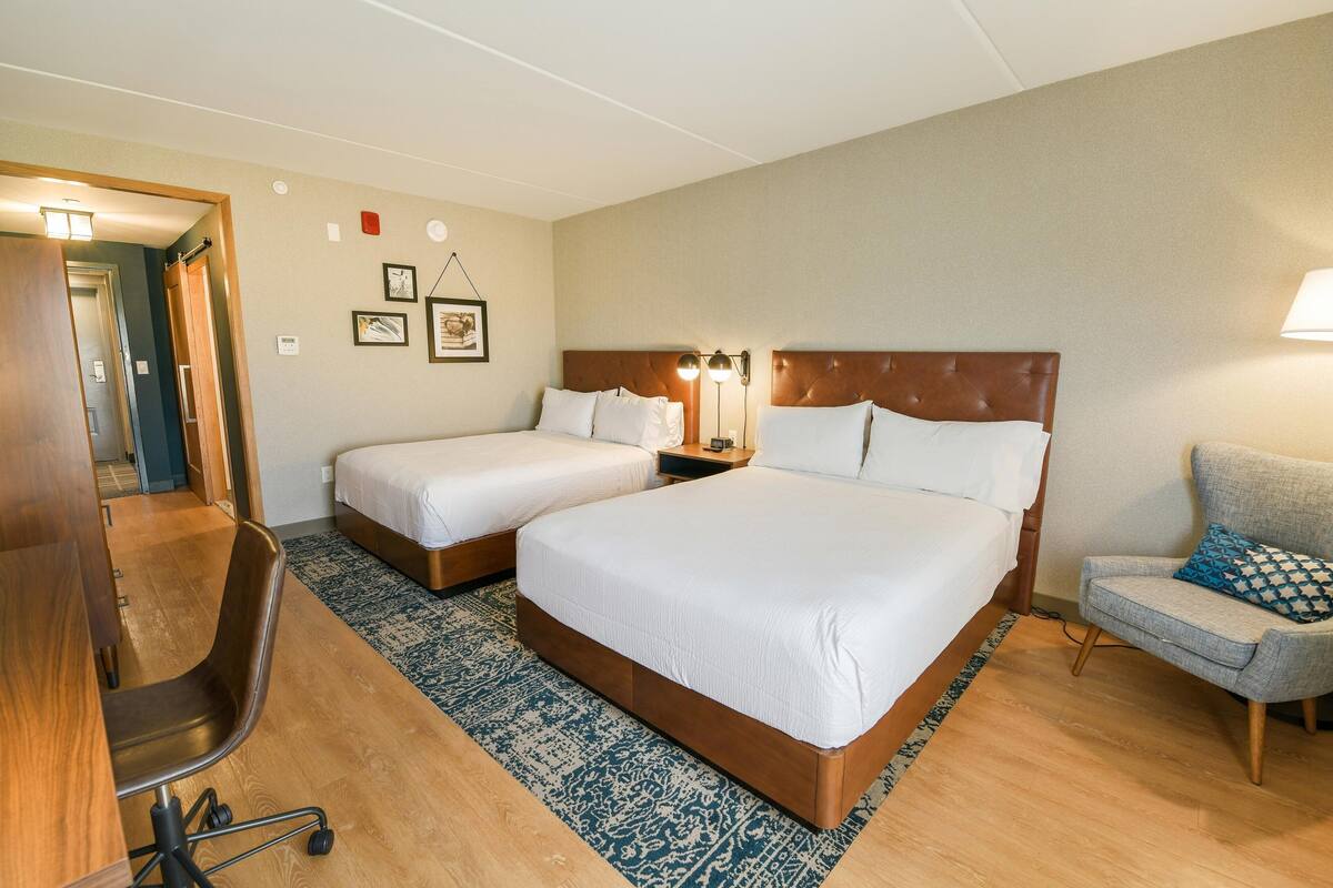 Ein Hotelzimmer mit zwei Betten, einem Schreibtisch, einem Stuhl und einer Lampe.