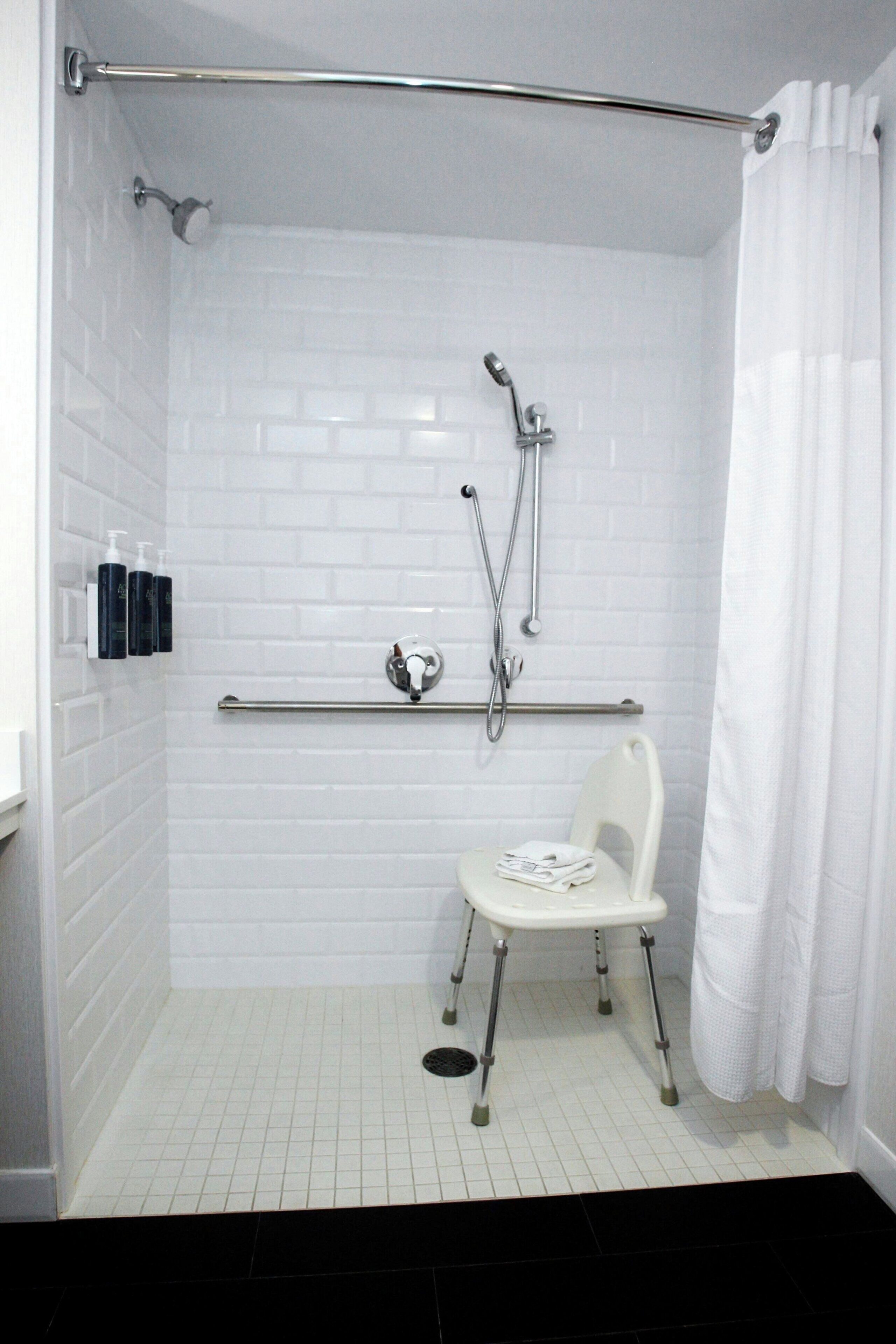 A shower with white tiled walls, a white chair, and a grab bar.