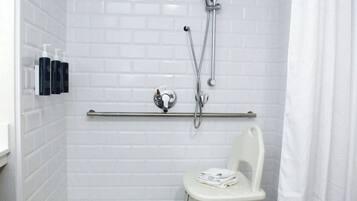 A shower with white tiled walls, a white chair, and a grab bar.