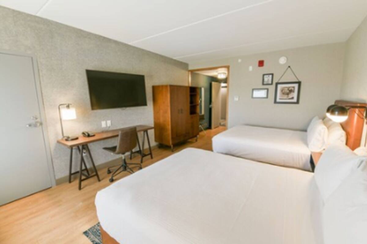 Ein Hotelzimmer mit zwei Betten, einem Schreibtisch, einem Stuhl, einem Fernseher und einem Kleiderschrank.