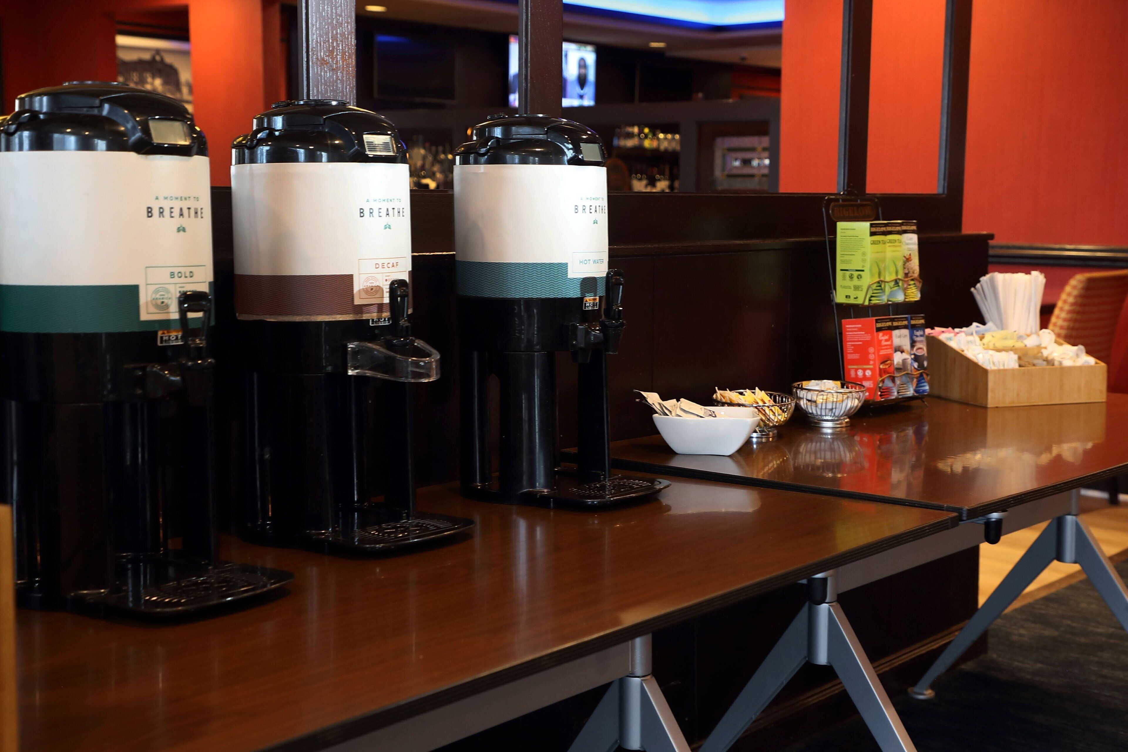 A coffee station with three coffee dispensers labeled "Breathe Bold" and "Breathe Decaf" in a hotel setting.