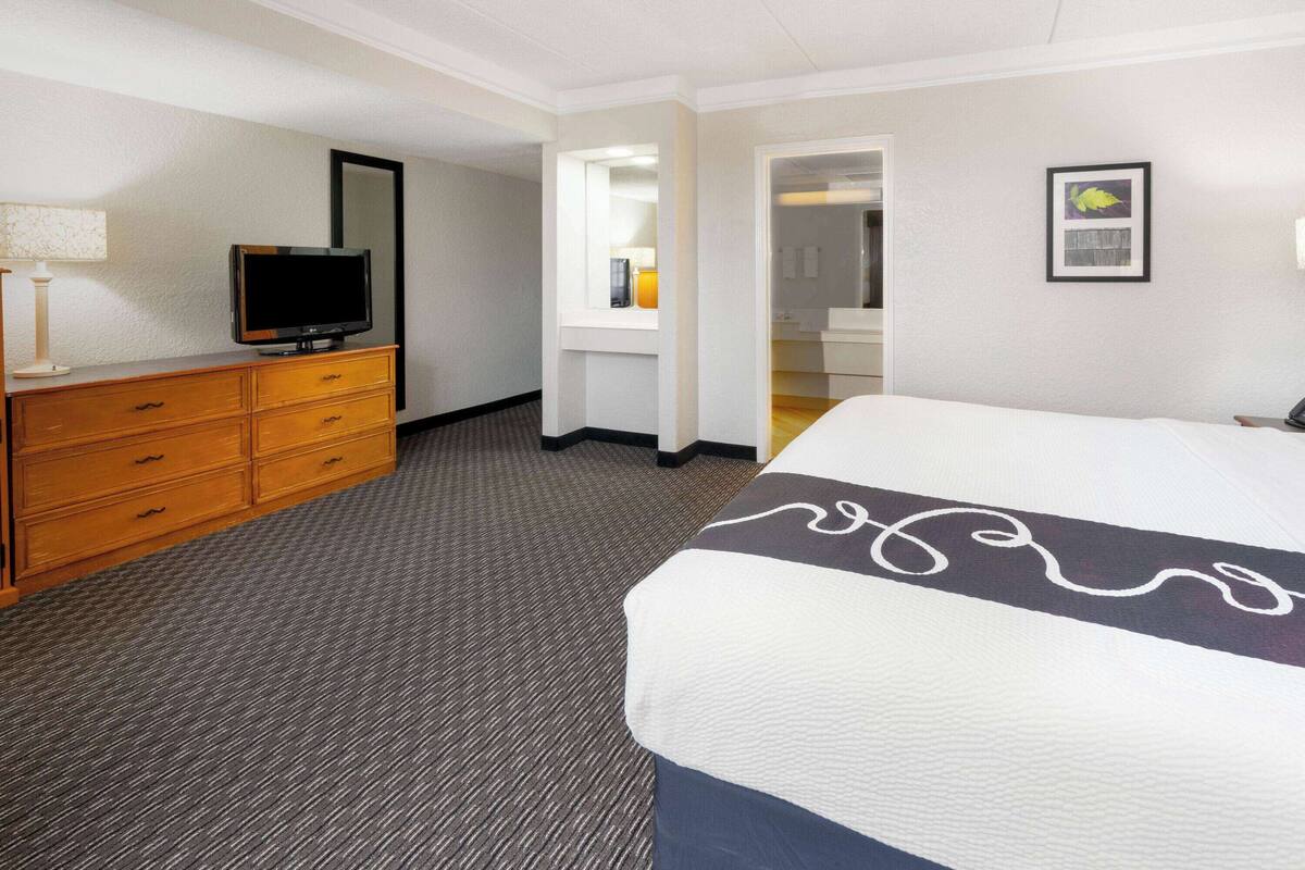Ein Hotelzimmer mit Bett, Schminktisch, Fernseher und Spiegel.