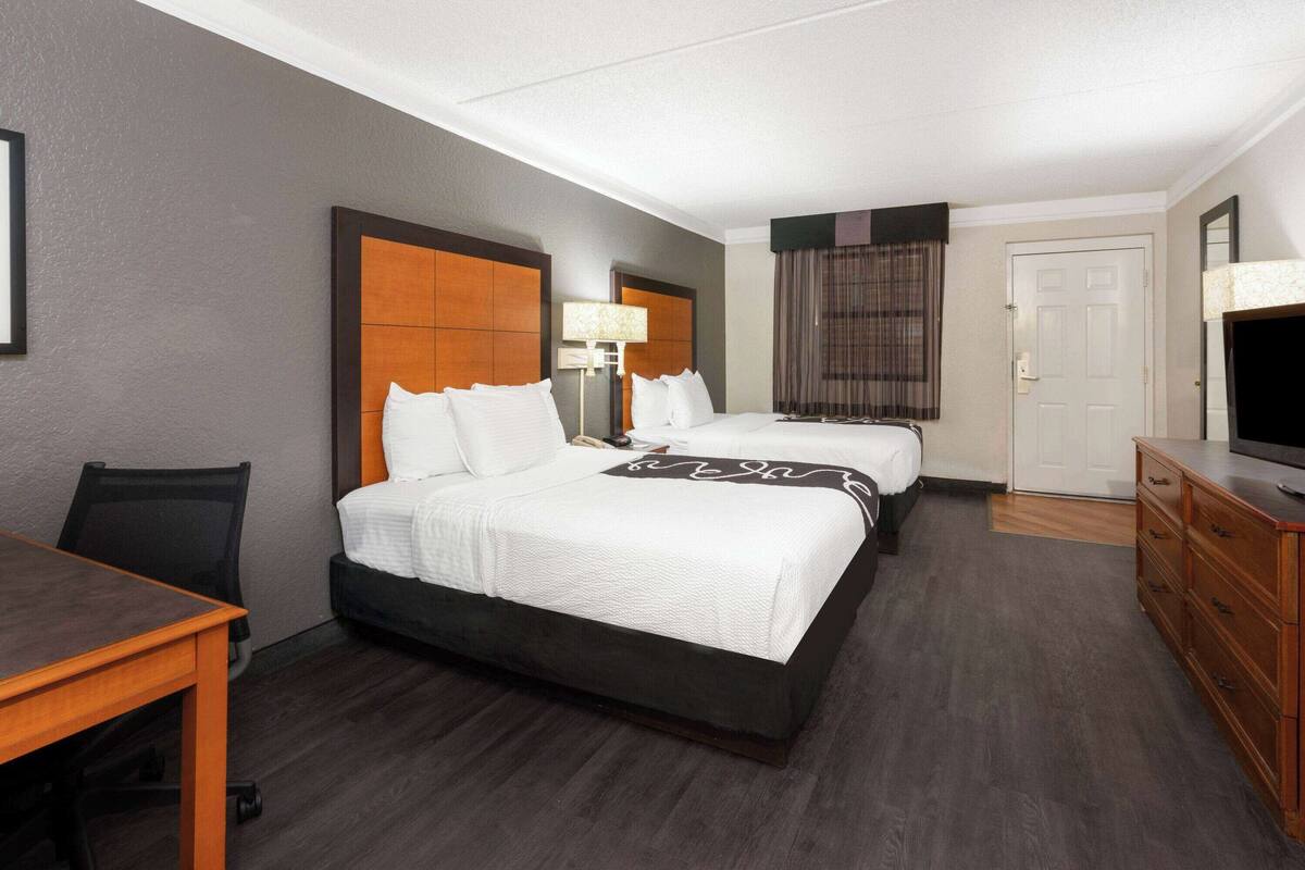 Ein Hotelzimmer mit zwei Betten, einem Schreibtisch, einem Fernseher und einem Schminktisch.