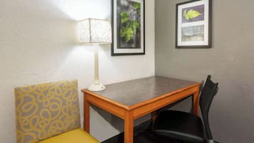 A small room with a wooden table, a black office chair, a yellow cushioned chair, and two framed pictures on the wall.