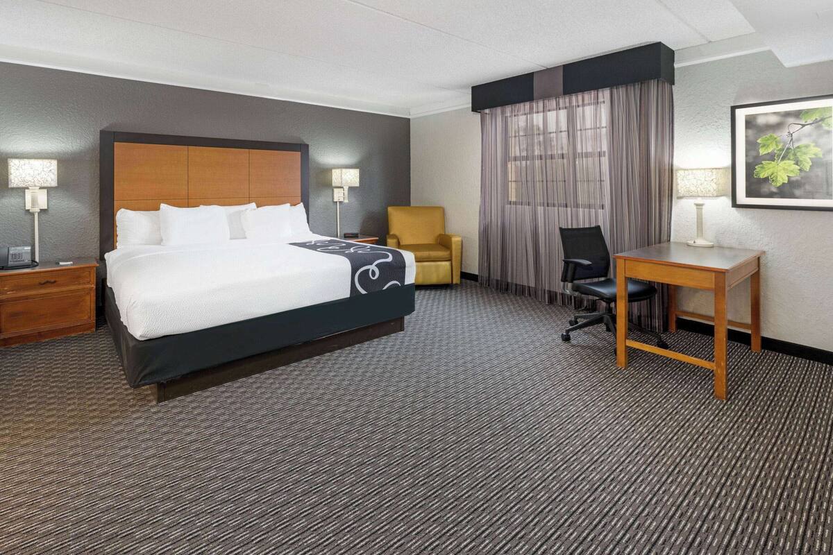 Ein Hotelzimmer mit einem großen Bett, einem Schreibtisch, einem Sessel und einem kleinen Tisch.