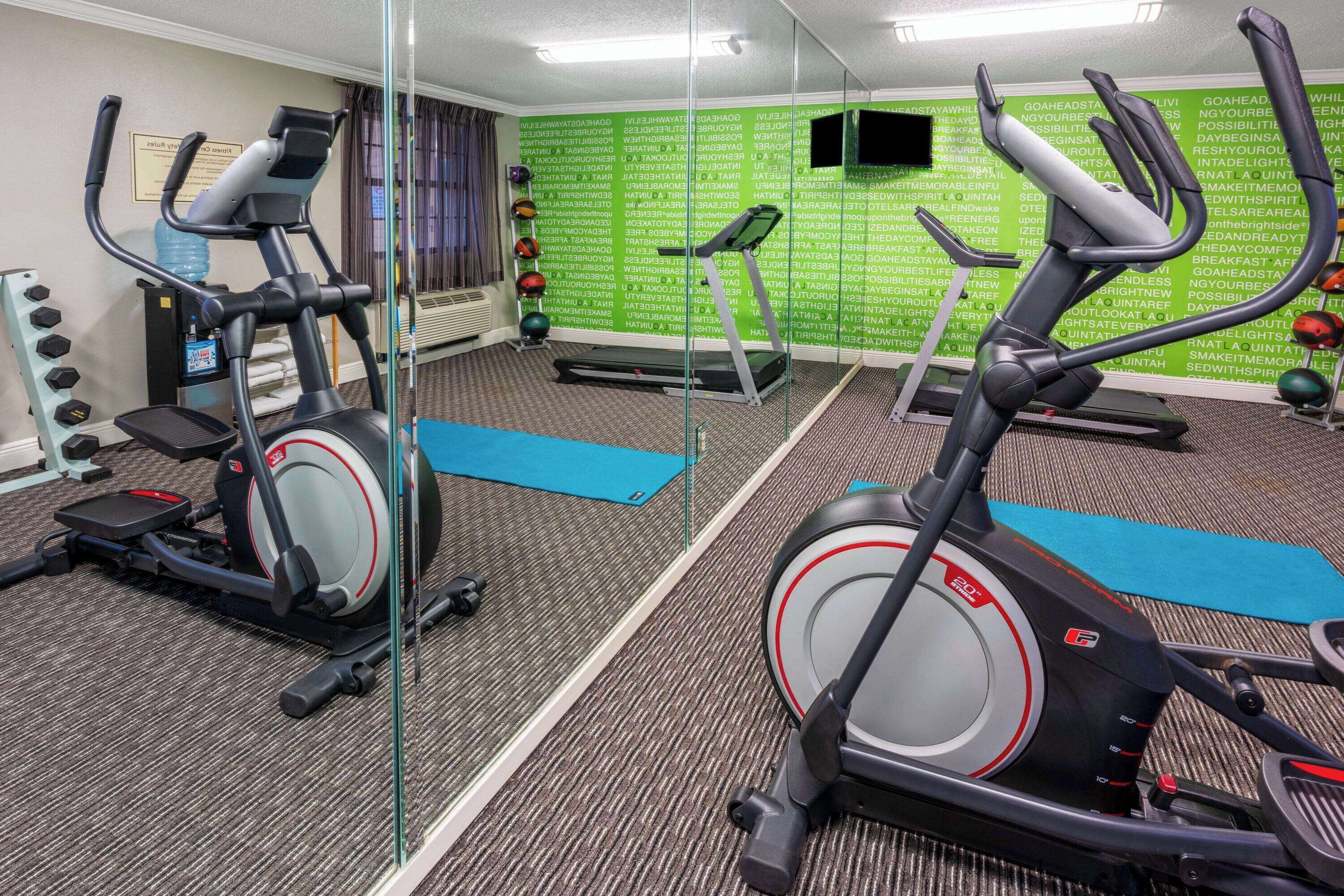 A gym with exercise equipment, a mirrored wall, and a green wall with motivational text.