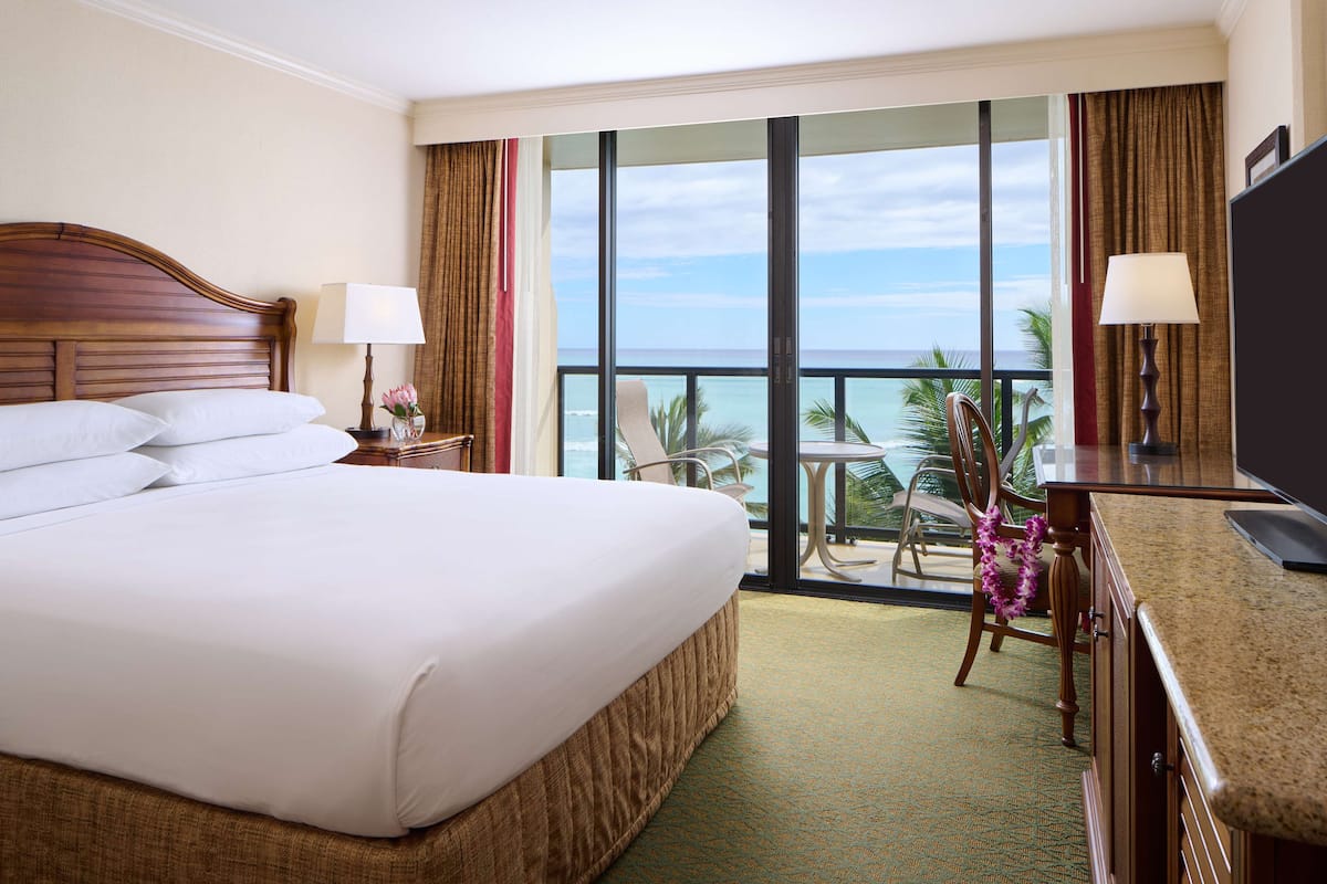 A hotel room with a large bed, a desk, a chair, and a view of the ocean.