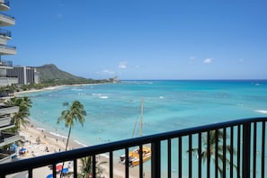 Blick auf einen Strand vom Balkon aus, mit blauem Himmel, Sandstrand und einem Boot im Wasser.