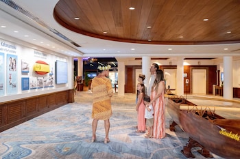 A hotel lobby with a wooden surfboard display, a reception desk, and a wall with informational posters. at OUTRIGGER Waikiki Beach Resort