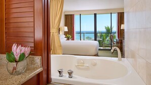 A hotel room with a large bathtub, a balcony with a view of the ocean, and a vase with flowers on the counter. - OUTRIGGER Waikiki Beach Resort (Honolulu)