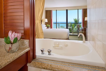 A resort pool with palm trees, lounge chairs, and a view of the ocean. at OUTRIGGER Waikiki Beach Resort