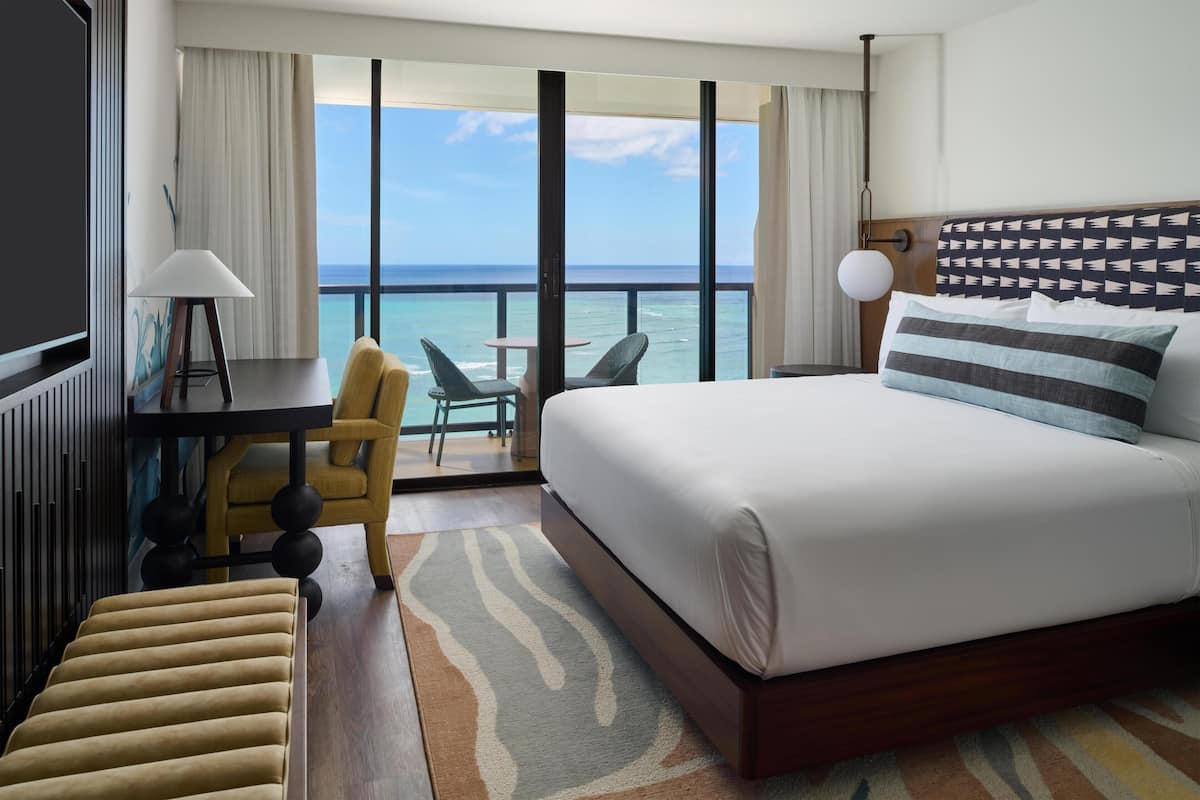 A hotel room with a large bed, a desk, a chair, and a view of the ocean.