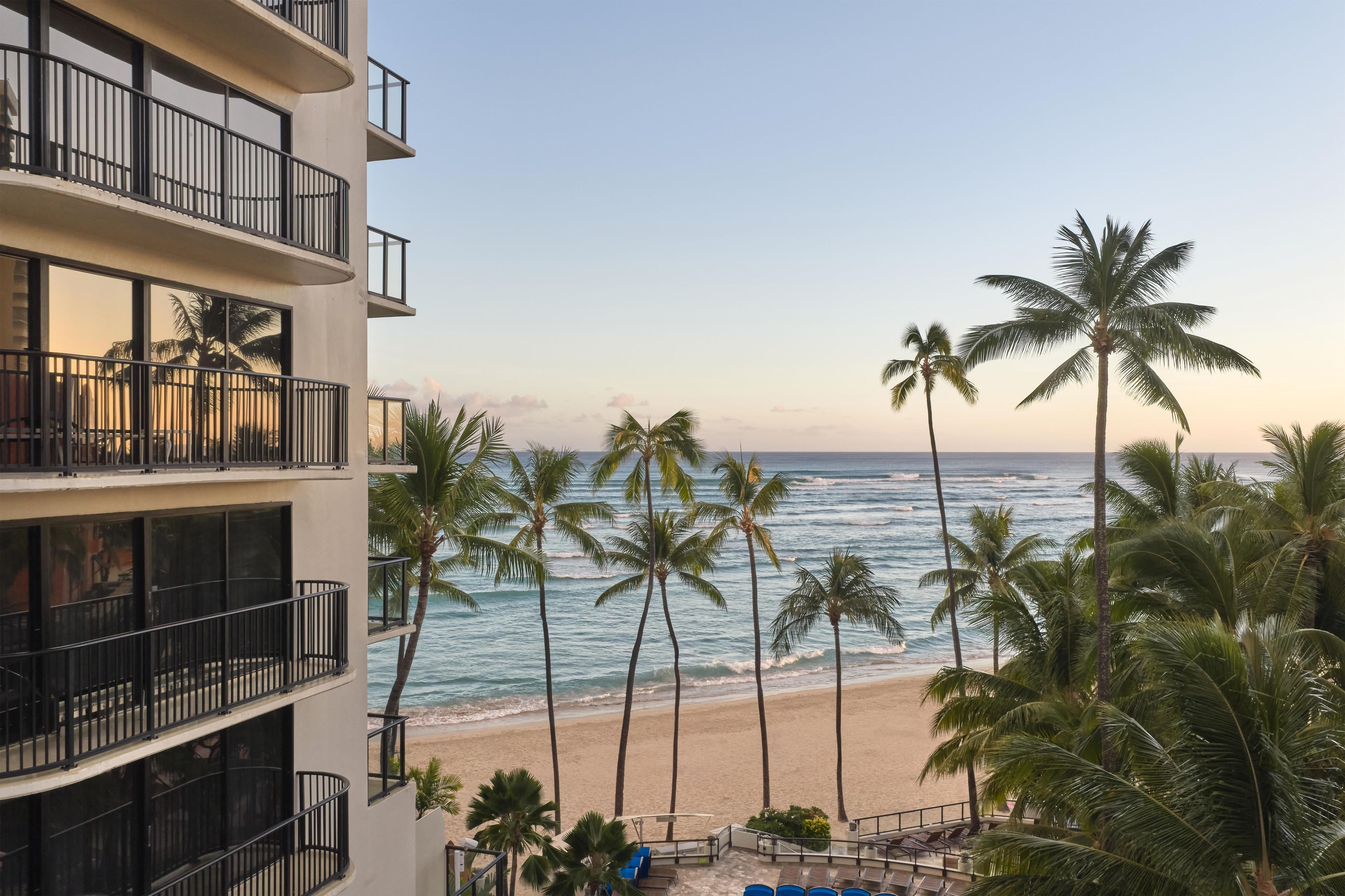 A beachfront hotel with multiple balconies overlooking the ocean and palm trees.