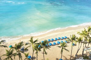 A beach with clear turquoise water, a sandy shore, and rows of blue umbrellas. - OUTRIGGER Waikiki Beach Resort (Honolulu)