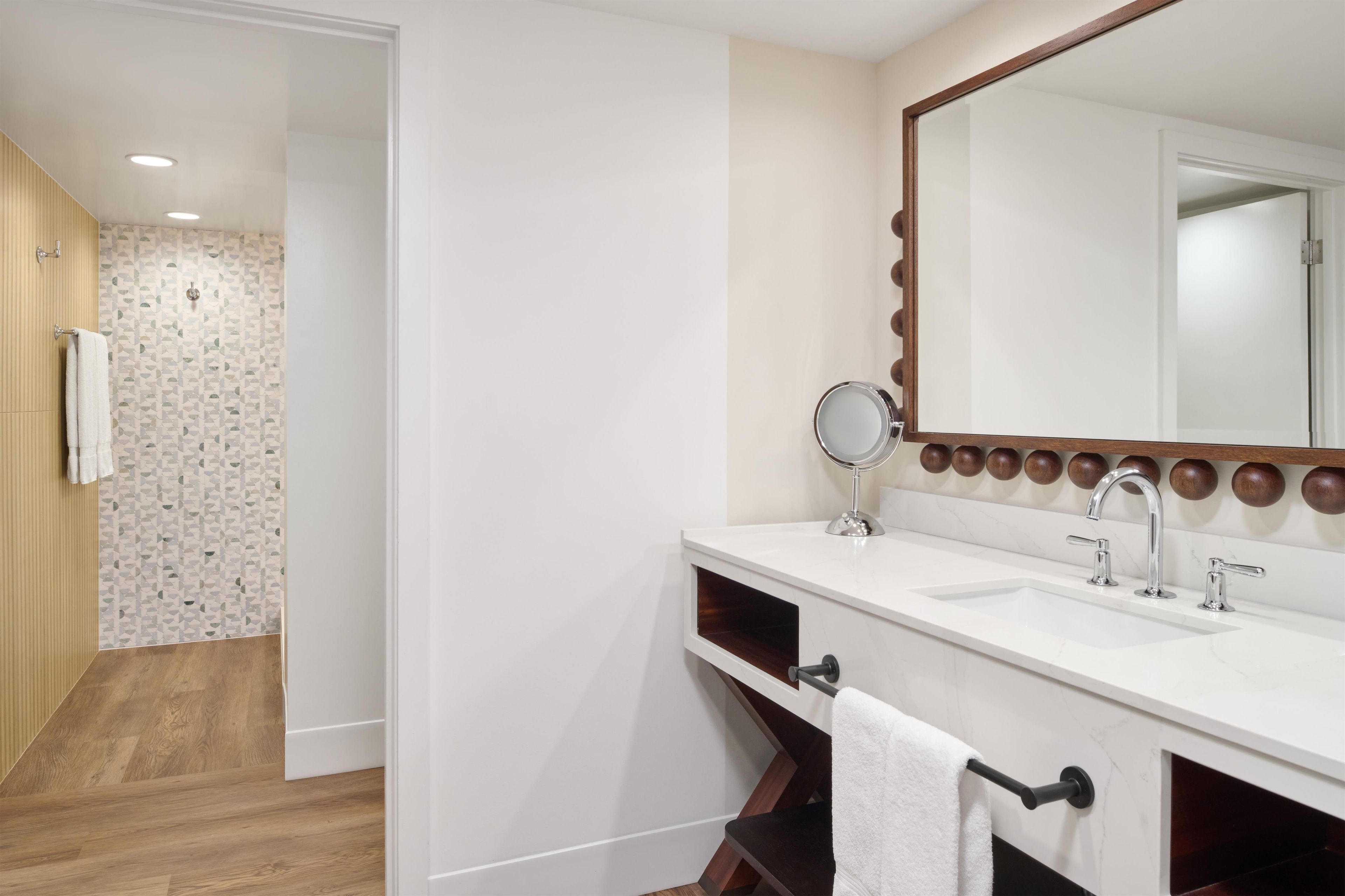 A bathroom with a white sink, a round mirror, and a wooden vanity.