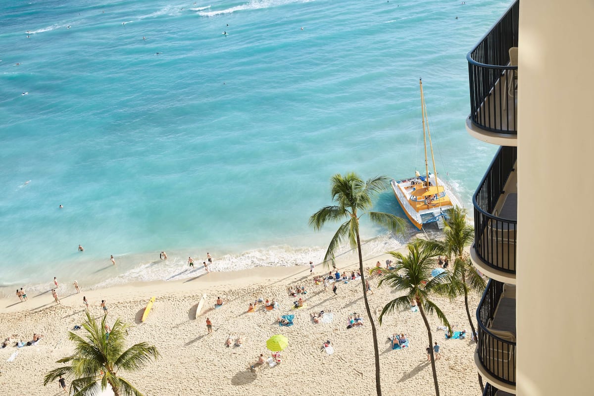 A beach with palm trees, a boat, and people on the sand.