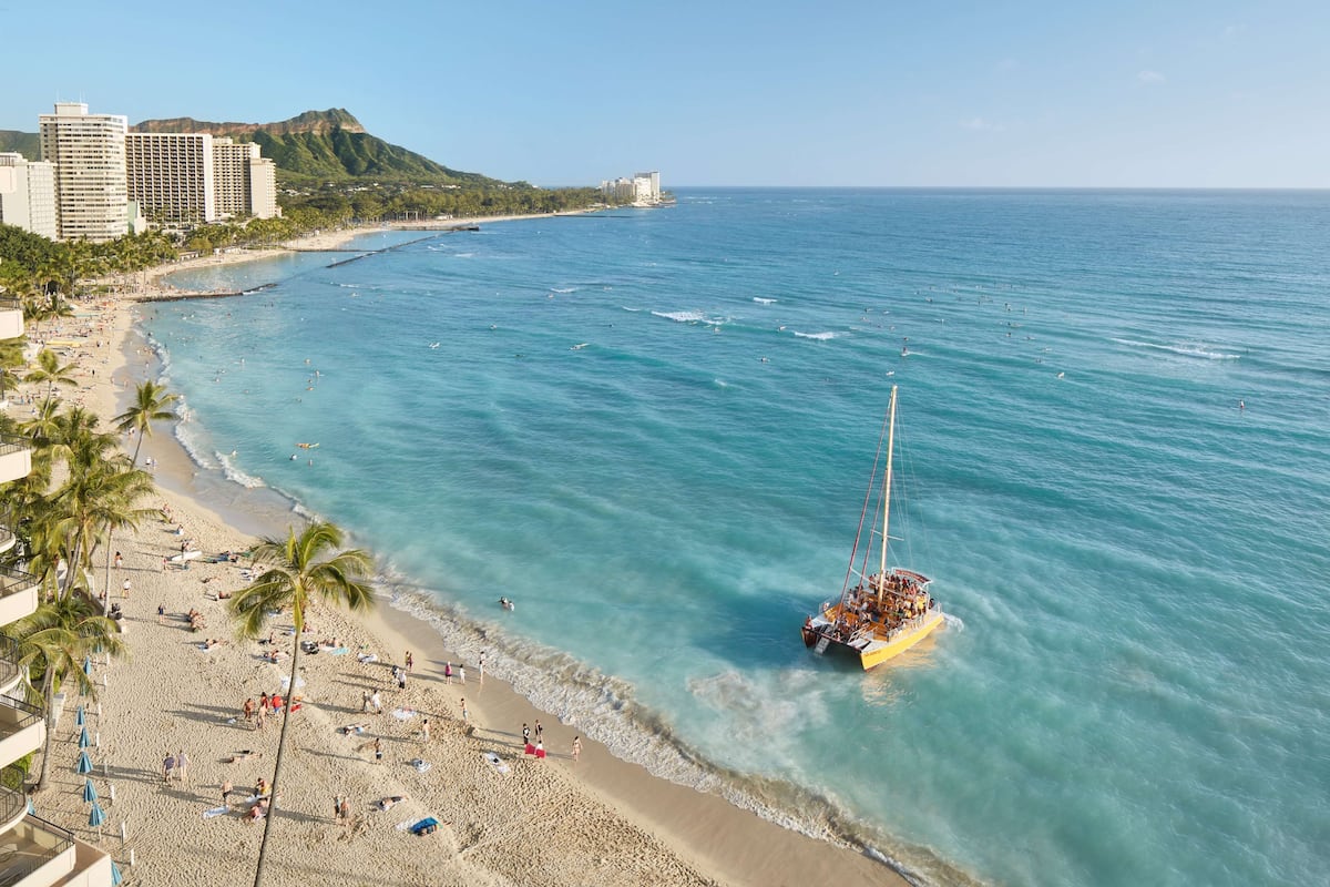 A beach with a boat, palm trees, and buildings in the background.