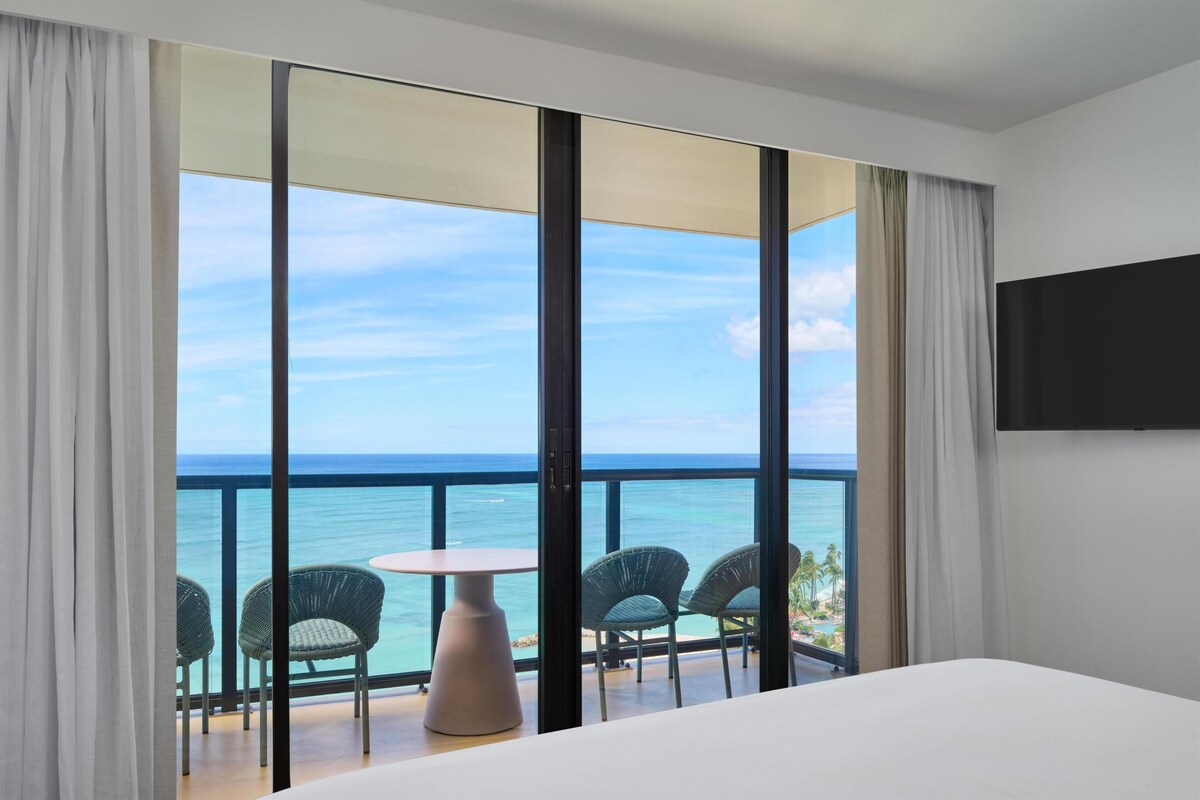 A hotel room with a balcony, a bed, and a view of the ocean.