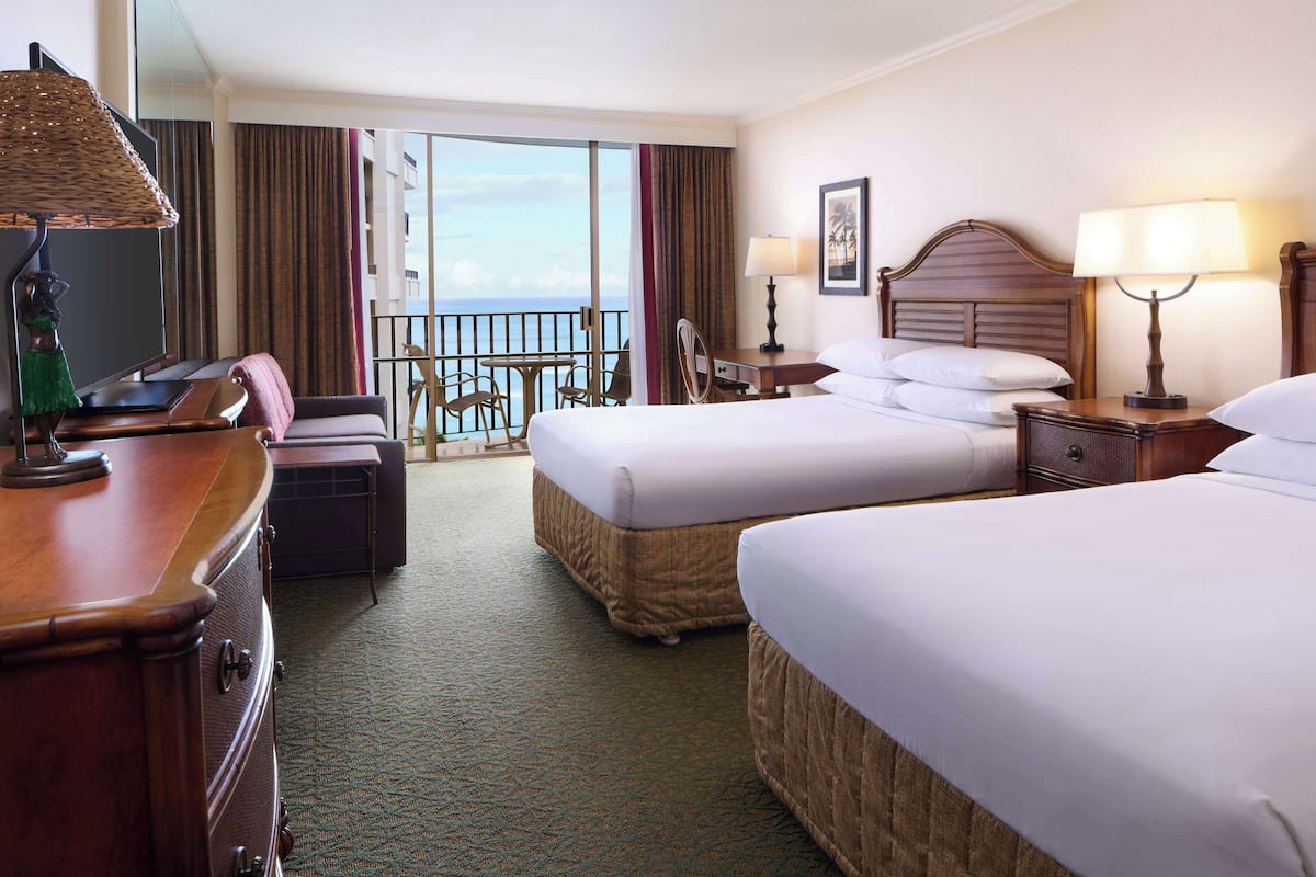 A hotel room with two beds, a desk with a lamp, a chair, a dresser, and a balcony with a view.