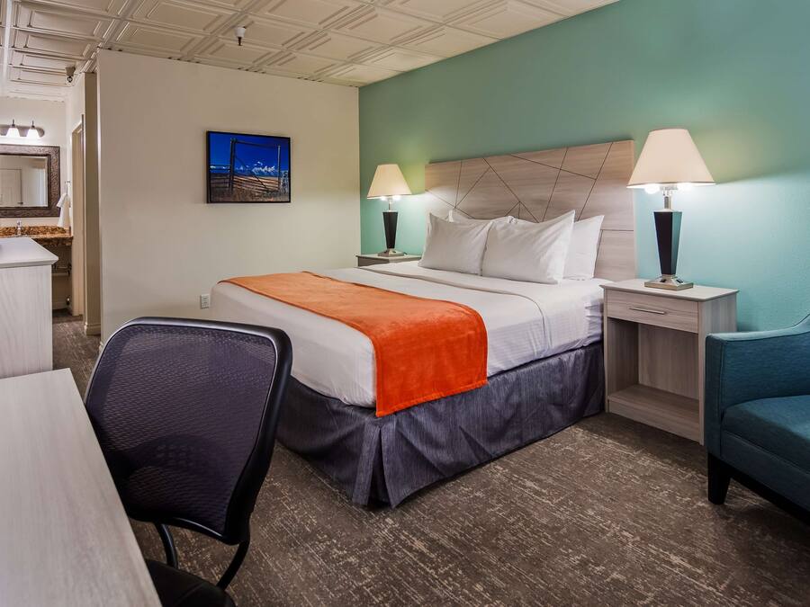 A hotel room with a bed, desk, chair, and a blue armchair.