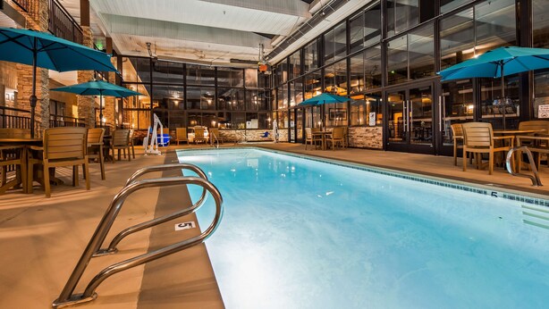 An indoor swimming pool with clear water, surrounded by wooden chairs and tables, and blue umbrellas.