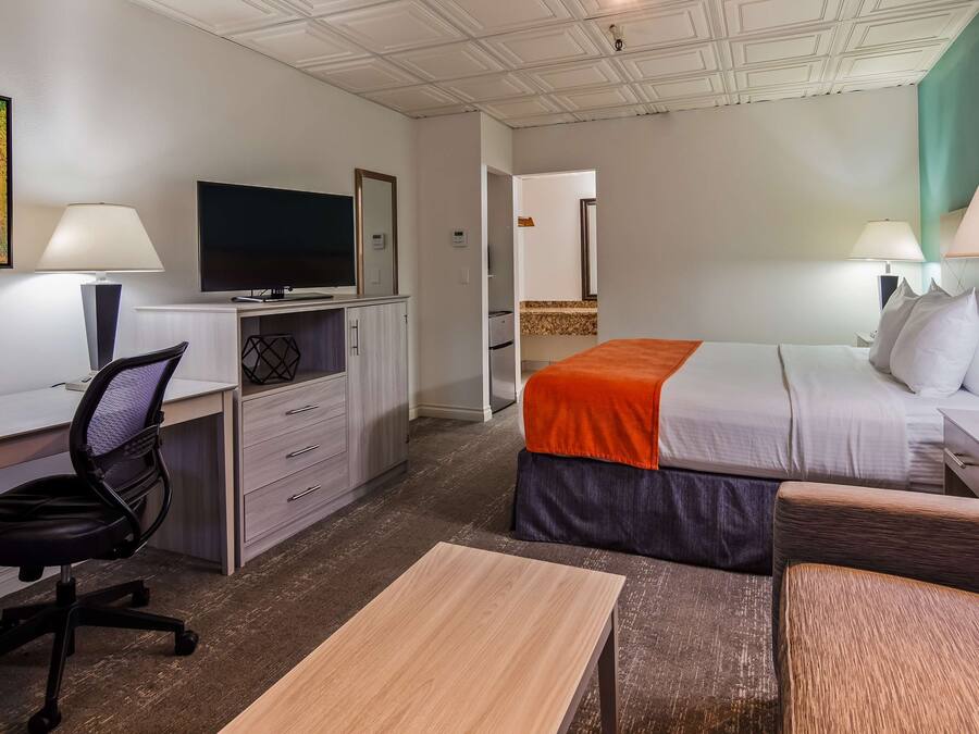 A hotel room with a desk, chair, bed, bedside tables, lamps, and a TV.