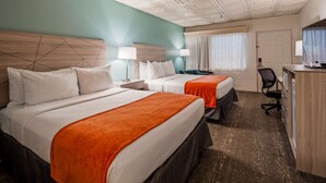 A hotel room with two beds, a desk, a chair, and a television.