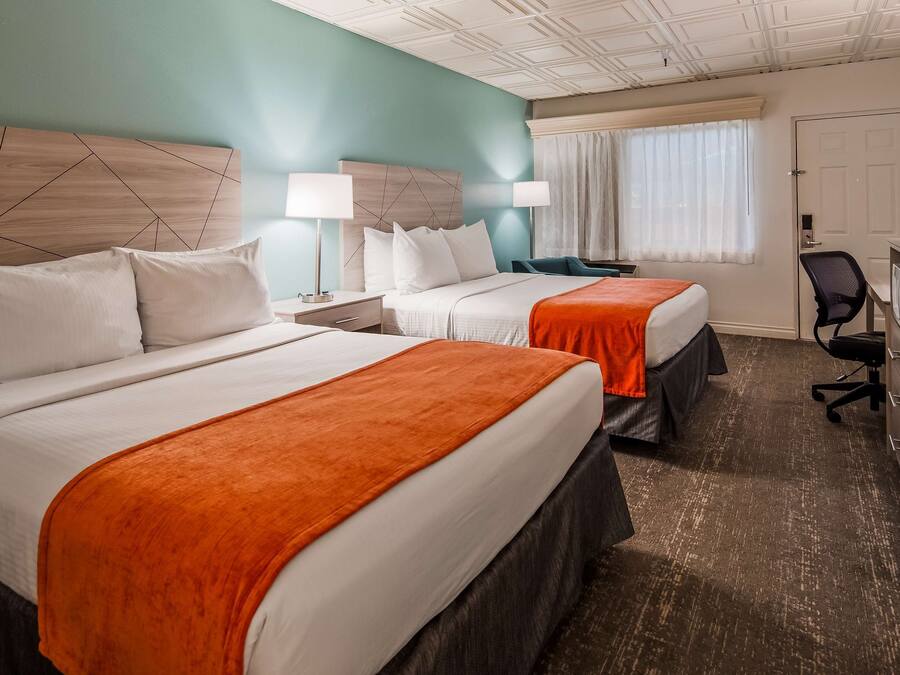 A hotel room with two beds, a desk, a chair, and a television.