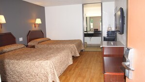 Habitación de hotel con dos camas, piso de madera, baño con lavamanos y espejo, y televisión montada en la pared.