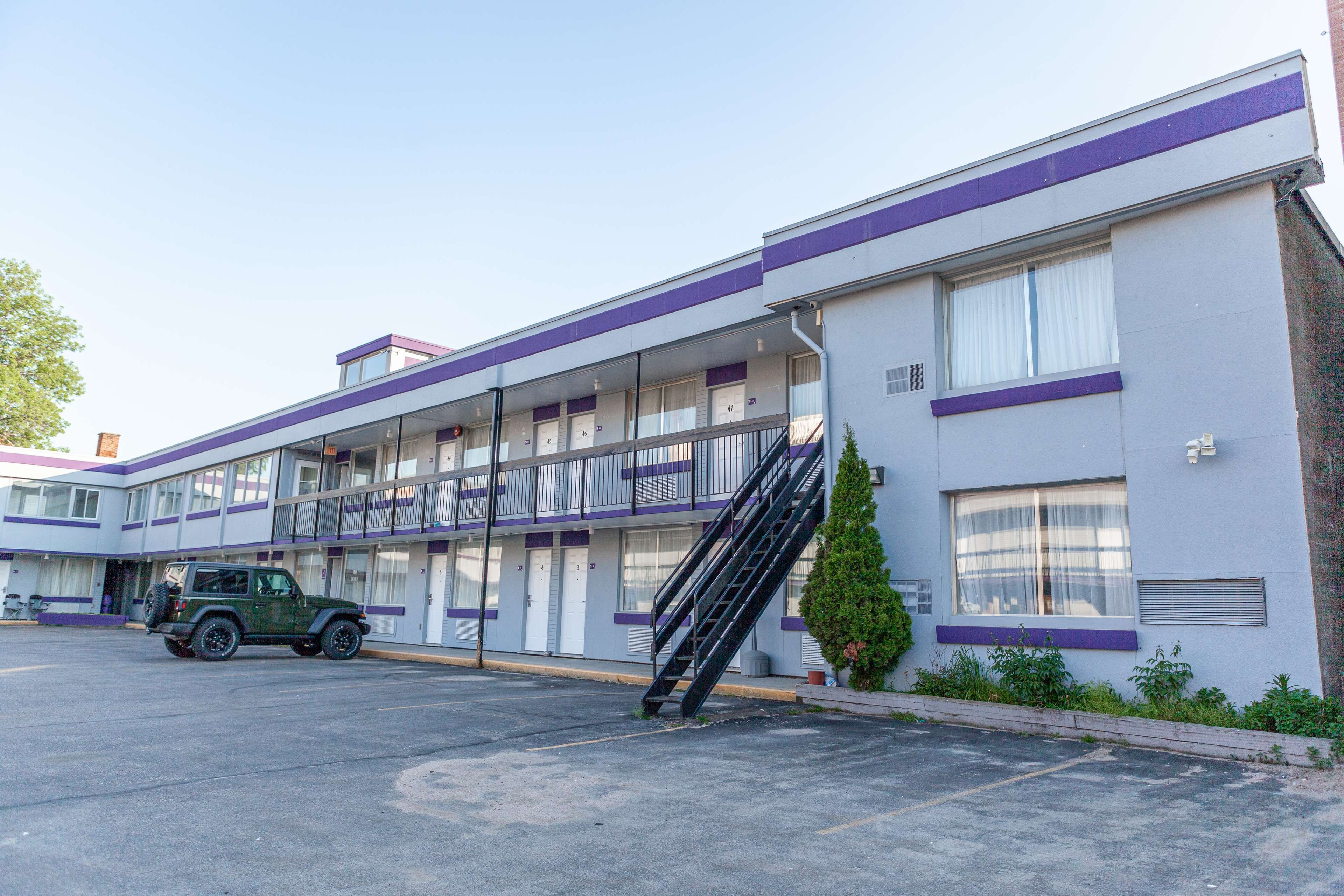 A motel with a two-story structure, a parking lot, and a green SUV parked in front.