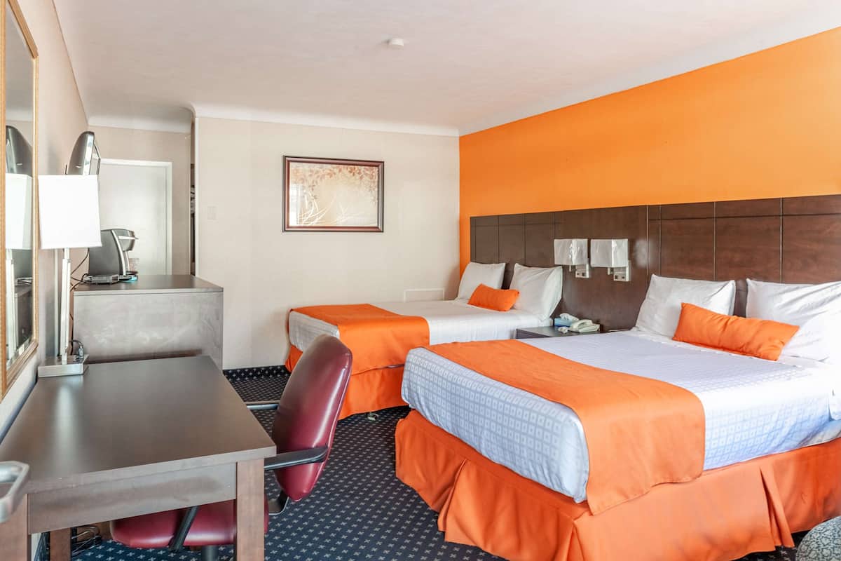 Habitación de hotel con dos camas, un escritorio, una silla y un espejo.
