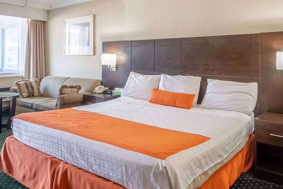 Habitación de hotel con una cama grande, un sofá, una mesita y un ventanal con cortinas.